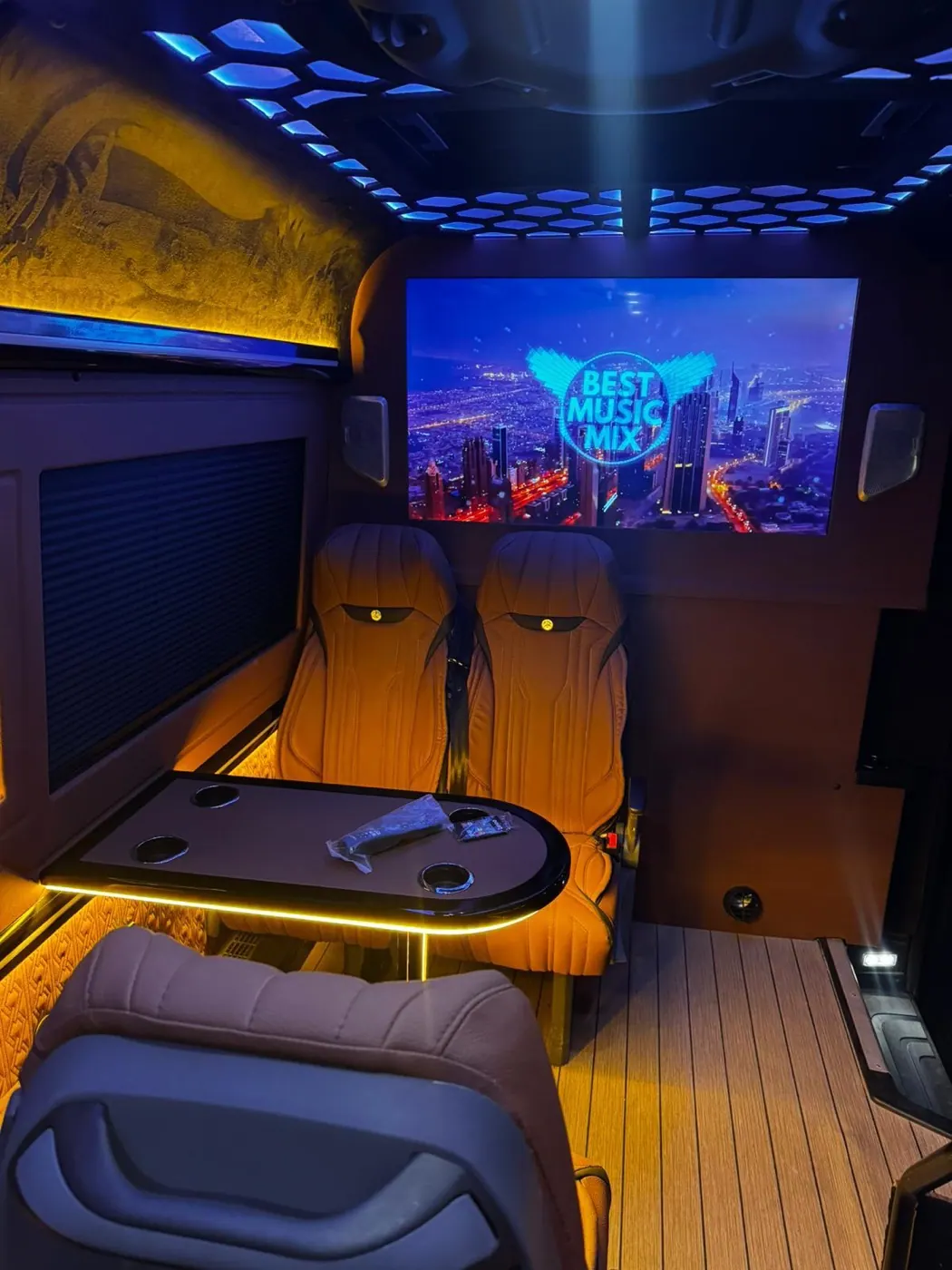 VIP transfer aracının deri koltukları, ahşap masası ve büyük ekran eğlence sisteminin genel görünümü